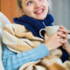 Young woman in scarf under blanket smiling in domestic interior